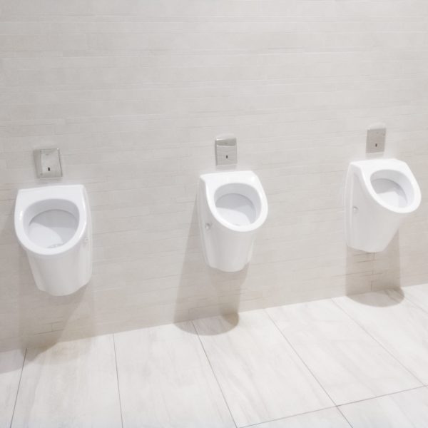 Row of three procelain urinals in clean efficient modern white tiled public men's washroom